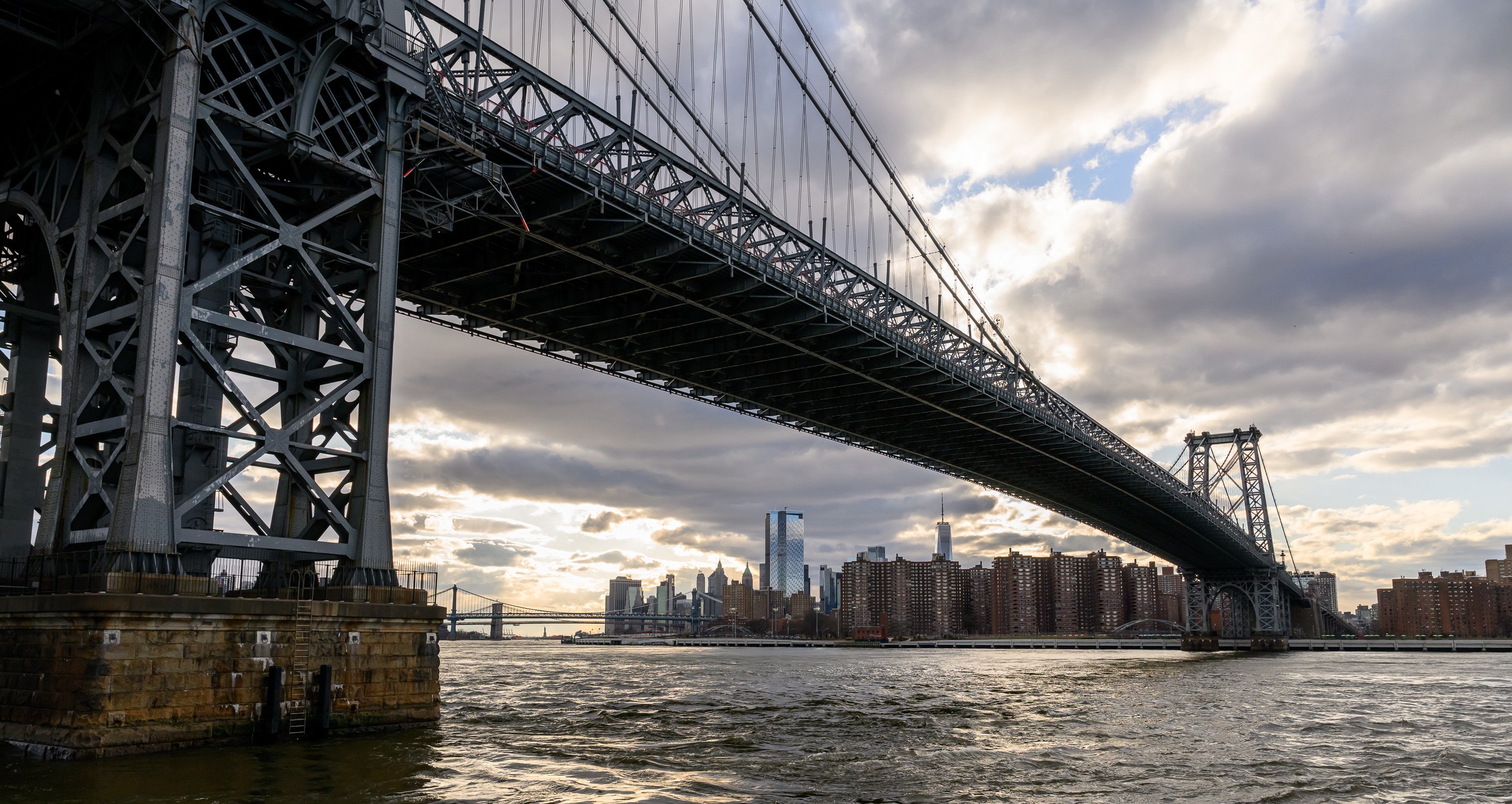 The Williamsburg Bridge with the Manhattan and Brooklyn Bridges in the background and lower Manhattan on a partly cloudy day. ©Sean Sime