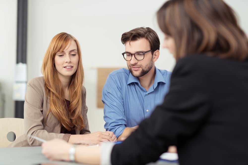 Broker making a presentation to a young couple showing them a document which they are viewing with serious expressions Broker making a presentation to a young couple showing them a document which they are viewing with serious expressions